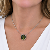 A close-up of a woman wearing a delicate silver chain necklace with a round bezel-set green gemstone pendant.