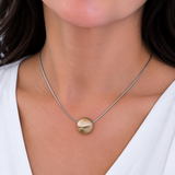 A close-up of a woman wearing a delicate silver chain necklace with a small, polished gold pendant.