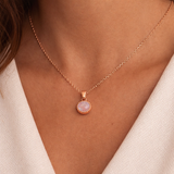 Rose gold necklace with a pink pendant on a person wearing a white top.