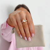 Hand holding a small beige pouch with a gold ring on a plain background