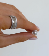 Hand holding a pearl earring against a plain background