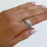 Hand wearing a silver ring with a pearl on a light background