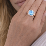 Close-up of a hand wearing a square halo ring with a blue gemstone.