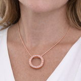 Rose gold necklace with a circular pendant worn by a person against a white background