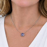 A close-up of a woman wearing a delicate silver chain necklace with a small round bezel-set purple gemstone pendant.