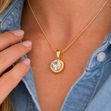 Gold necklace with a round pendant worn by a person in a denim shirt.