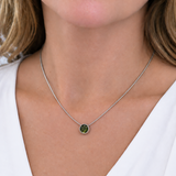 A close-up of a woman wearing a delicate silver chain necklace with a small round pendant featuring a green stone.
