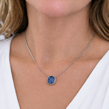 A close-up of a woman wearing a delicate silver chain necklace with a round blue pendant, styled with a white V-neck top.