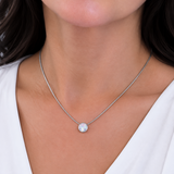 A close-up of a woman wearing a delicate silver chain necklace with a single round, milky white pearl pendant.