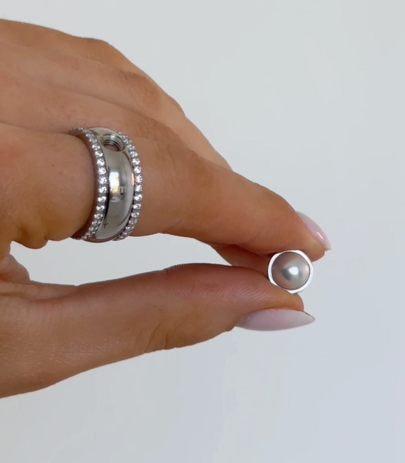 Hand holding a pearl earring against a plain background