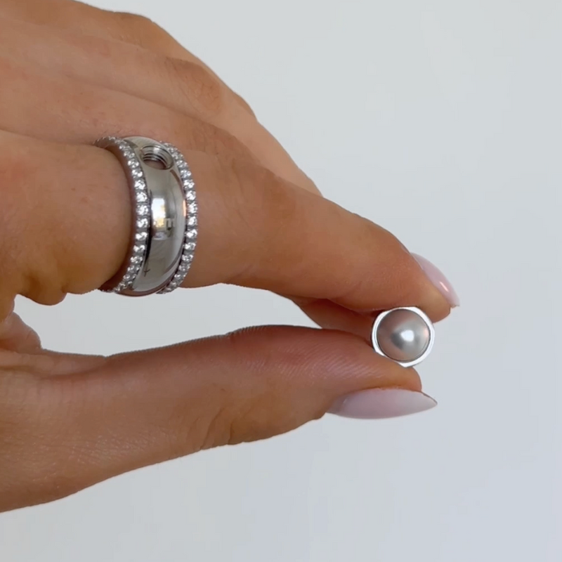 Hand holding a pearl earring against a plain background