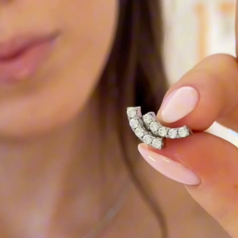 Close-up of a diamond earring held by a hand with pink nail polish.