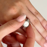 Close-up of a hand wearing a ring with a pearl-like center on a plain background