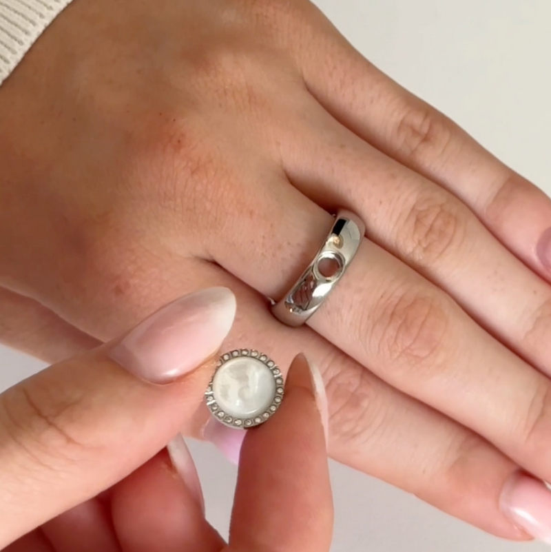 Close-up of a hand wearing two silver rings with a white stone on a light background