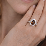 Close-up of a hand wearing an elegant ring with a brown oval gemstone and diamond halo