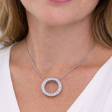 Silver necklace with a circular pendant worn by a person in a white top.
