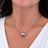 A close-up of a woman wearing a delicate silver chain necklace with a polished, spherical silver pendant.